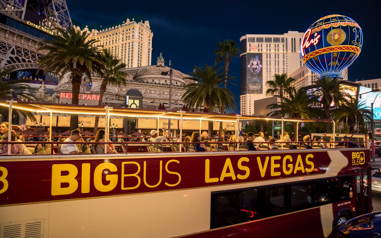 Open-top Big Bus tour in Las Vegas passing Paris Hotel and Casino at night.
