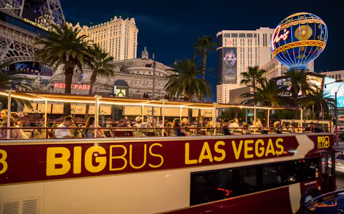 Open-top Big Bus tour in Las Vegas passing Paris Hotel and Casino at night.