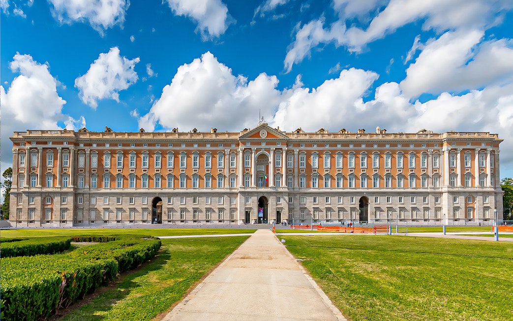 Royal Palace of Caserta facade with gardens under blue sky, Italy.