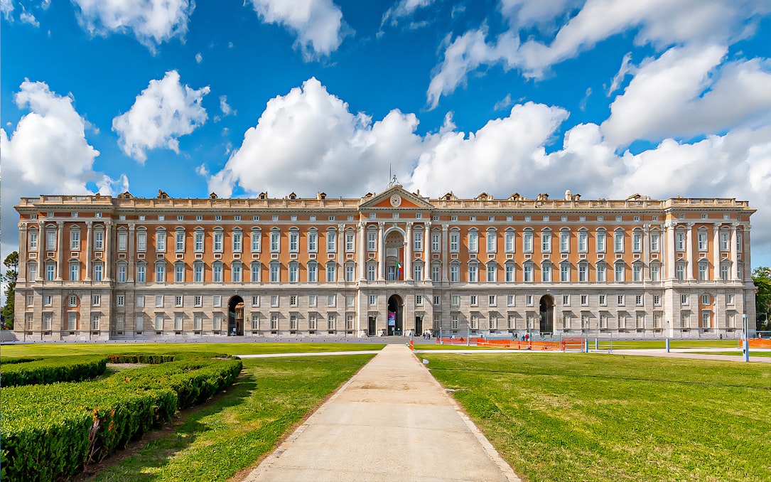 Royal Palace of Caserta facade with gardens under blue sky, Italy.