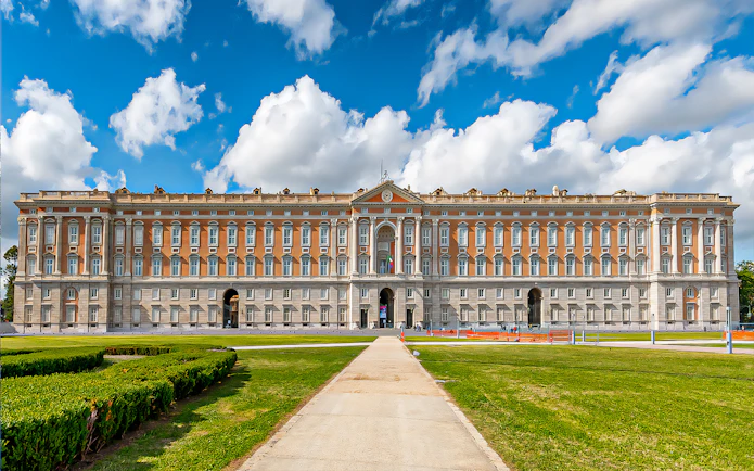 Royal Palace of Caserta facade with gardens under blue sky, Italy.