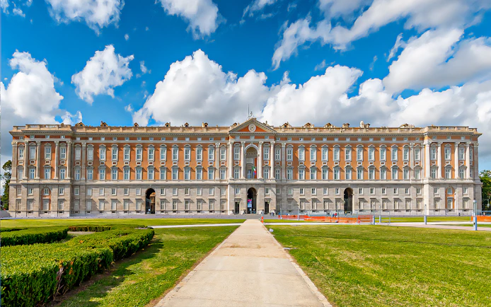 Royal Palace of Caserta facade with gardens under blue sky, Italy.