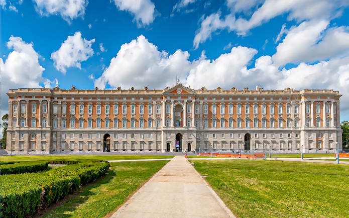 Royal Palace of Caserta facade with gardens under blue sky, Italy.