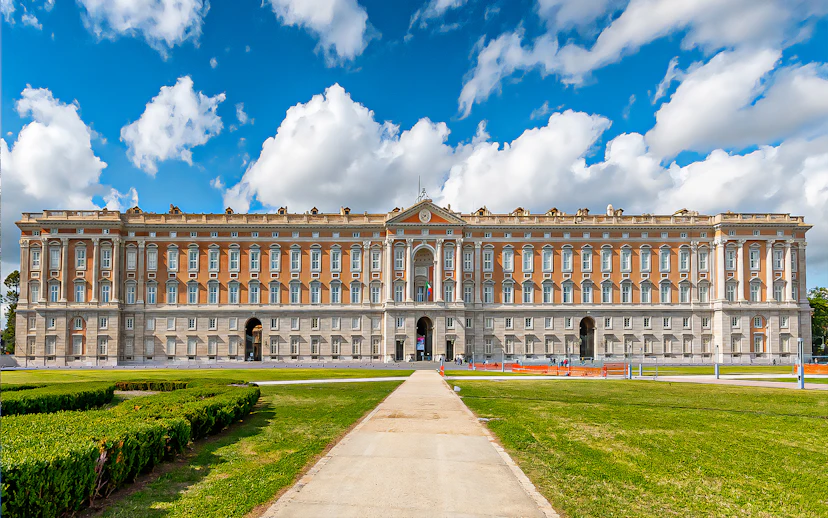 Royal Palace of Caserta facade with gardens under blue sky, Italy.