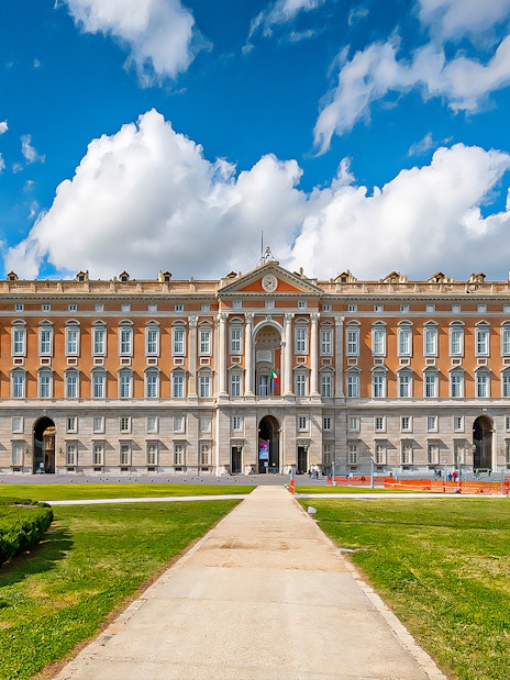 Royal Palace of Caserta facade with gardens under blue sky, Italy.