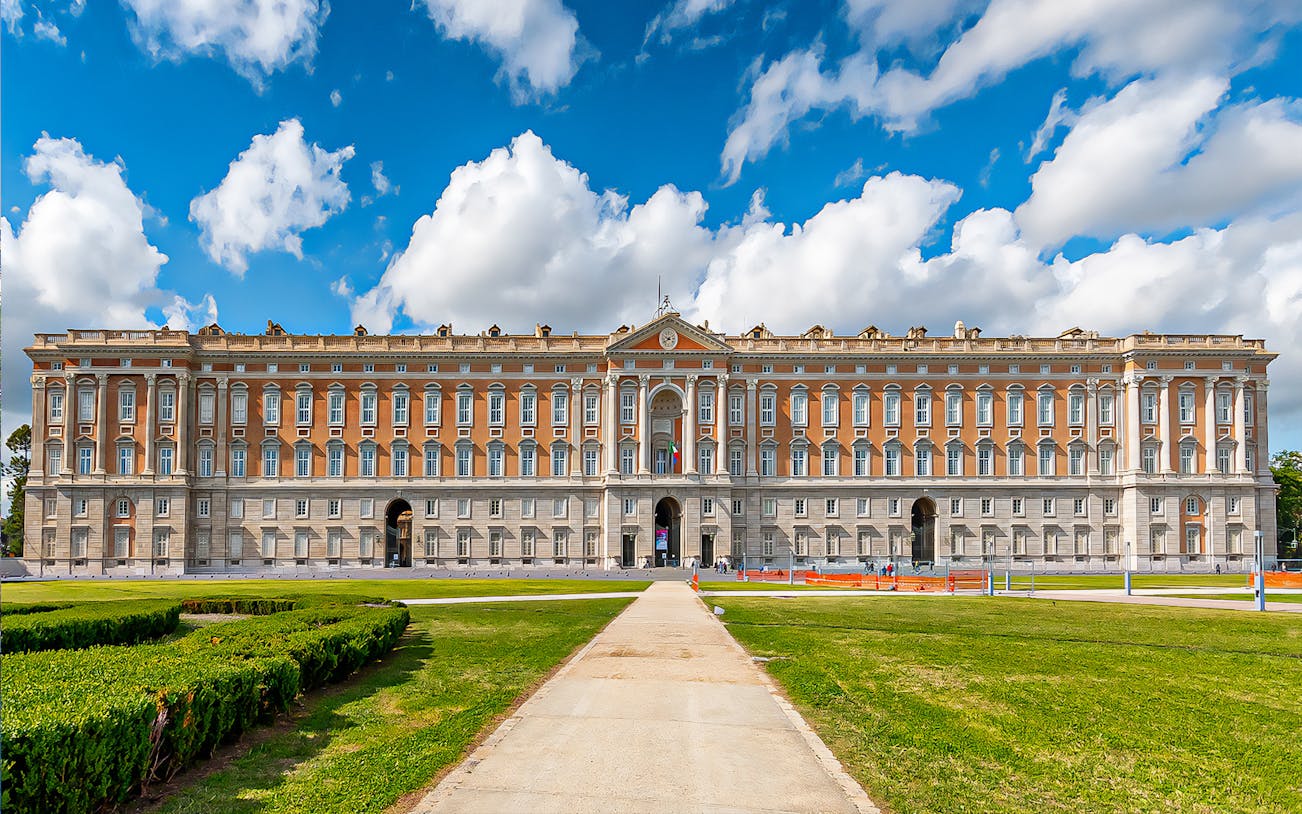 Royal Palace of Caserta facade with gardens under blue sky, Italy.