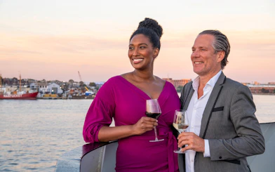 Couple enjoying wine on Long Beach dinner cruise deck at sunset.