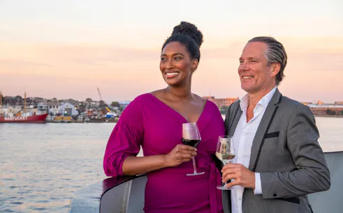 Couple enjoying wine on Long Beach dinner cruise deck at sunset.