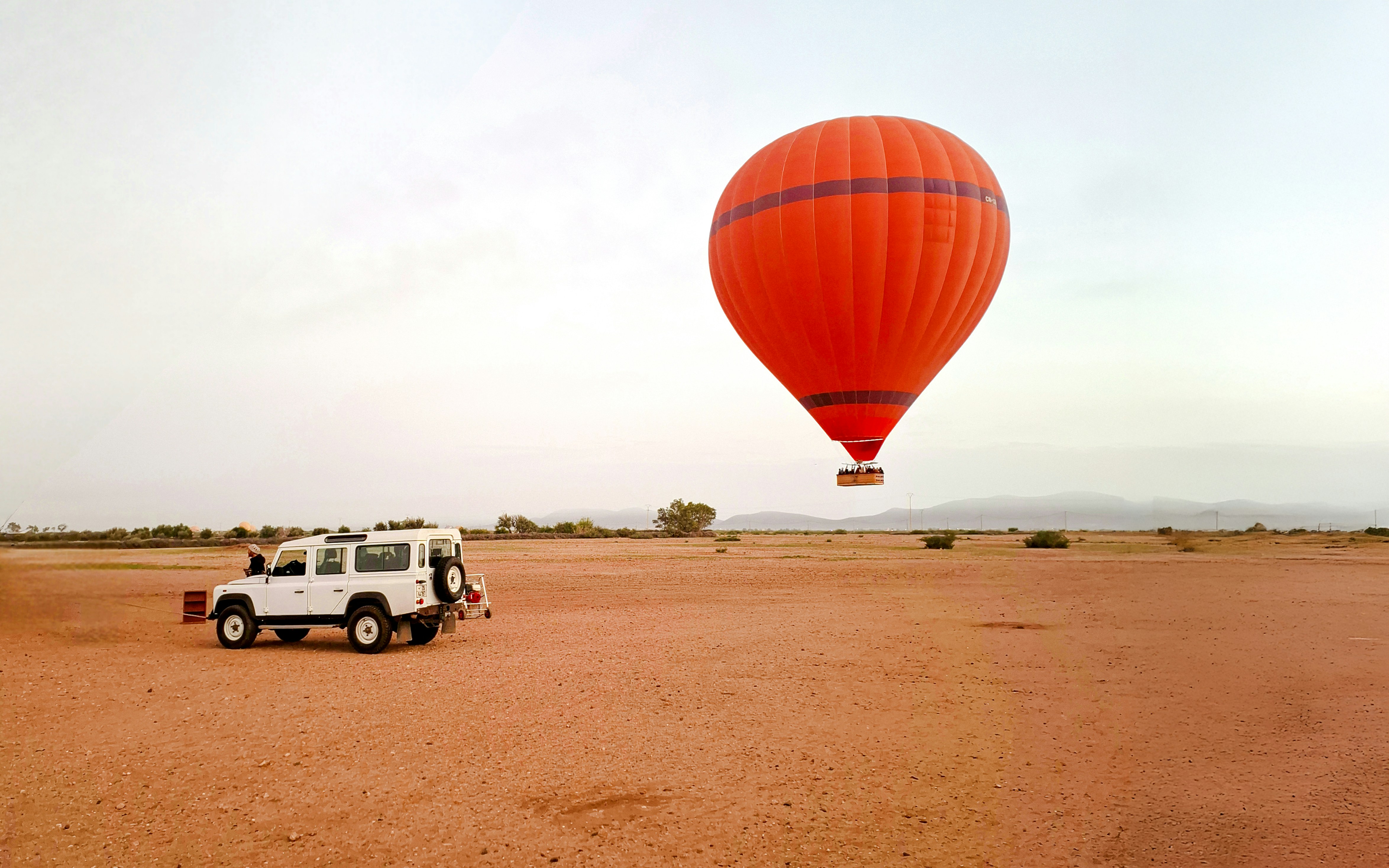 Crew inflating hot air balloon near vehicle in Marrakech desert.