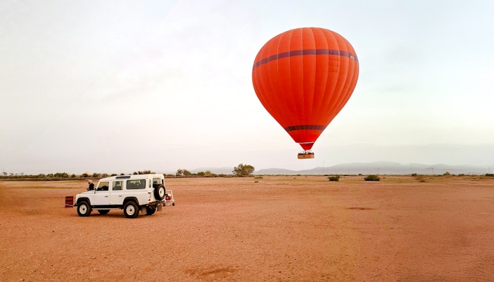 Crew inflating hot air balloon near vehicle in Marrakech desert.