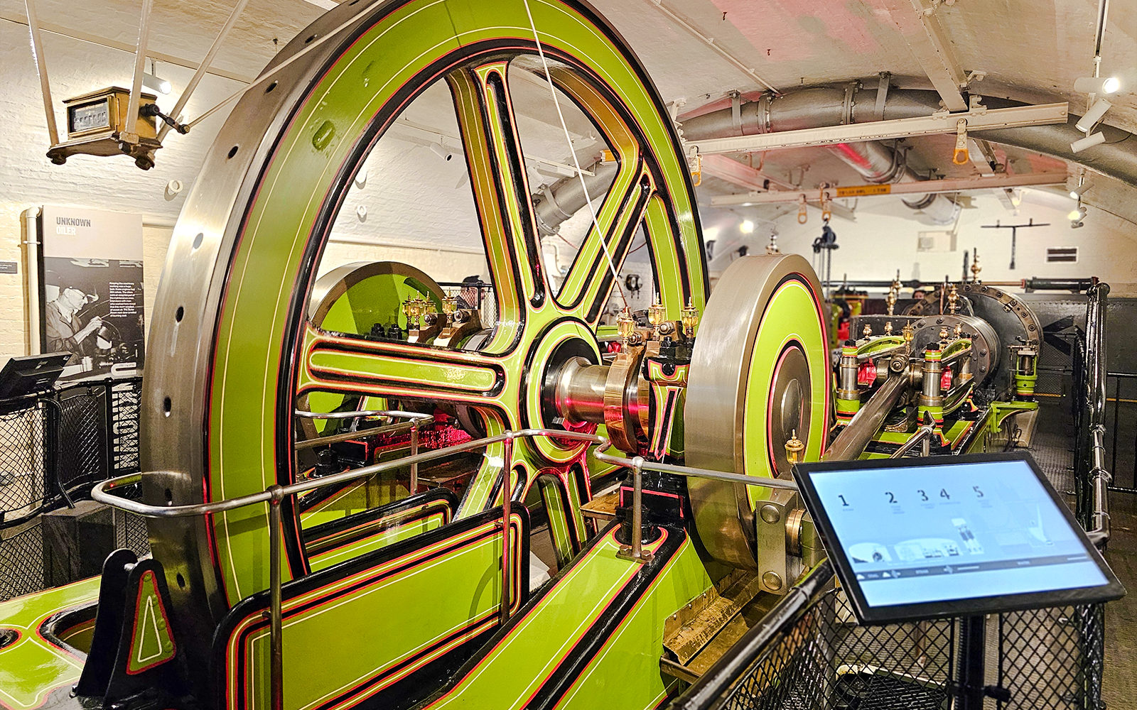 Engine room machinery at Tower Bridge, London, featuring large green and red wheels.