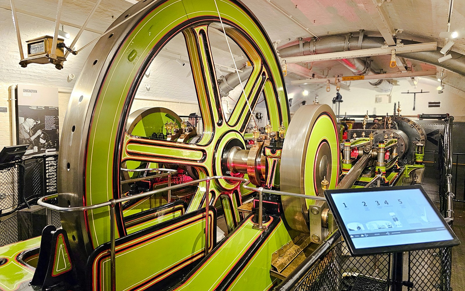 Engine room machinery at Tower Bridge, London, featuring large green and red wheels.