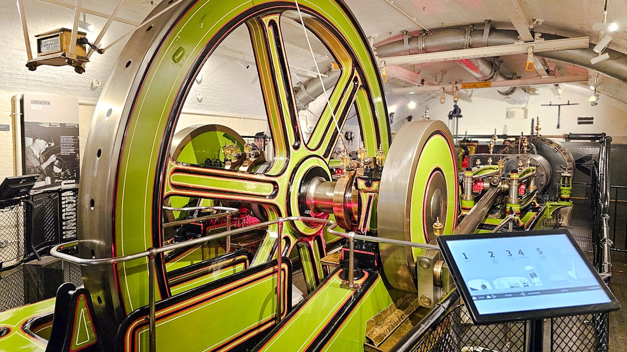 Engine room machinery at Tower Bridge, London, featuring large green and red wheels.