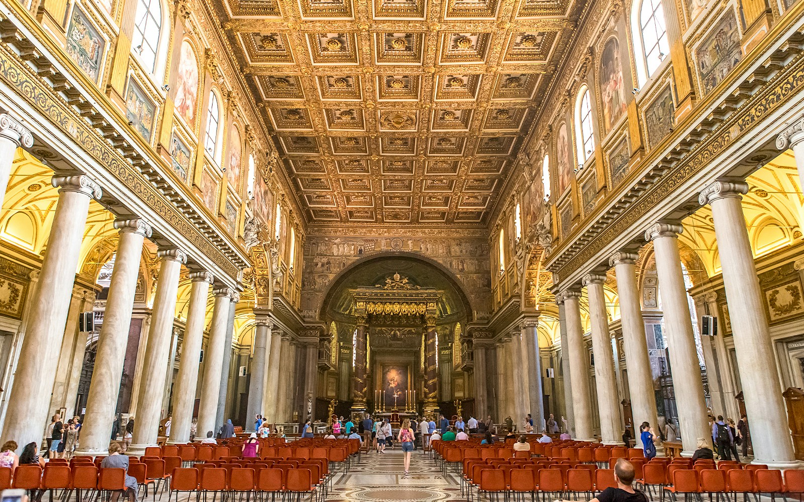 Visitors at the altar of Basilica Santa Maria Maggiore, Rome, with ornate ceiling and columns.