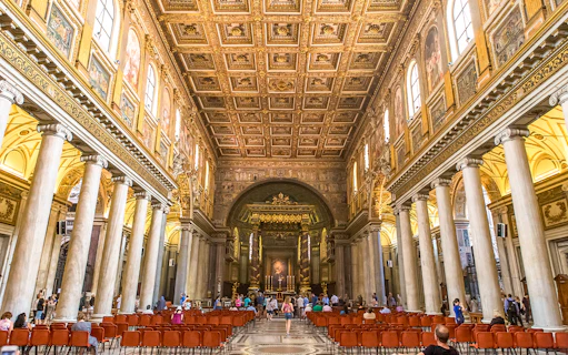 Visitors at the altar of Basilica Santa Maria Maggiore, Rome, with ornate ceiling and columns.