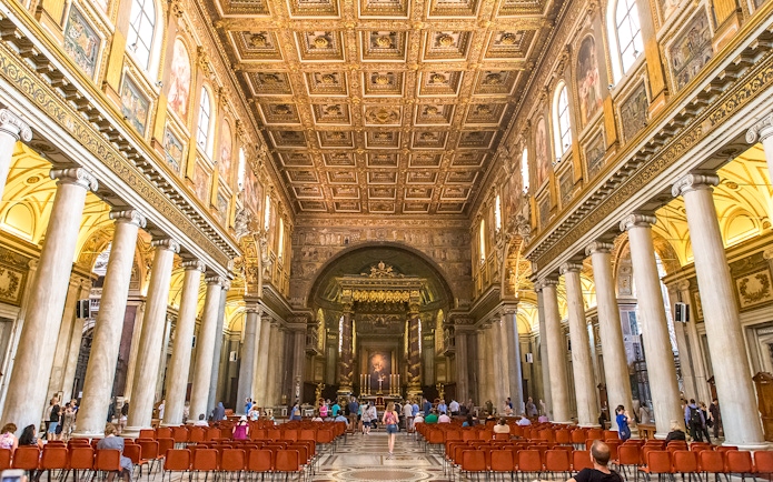 Visitors at the altar of Basilica Santa Maria Maggiore, Rome, with ornate ceiling and columns.