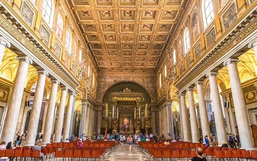Visitors at the altar of Basilica Santa Maria Maggiore, Rome, with ornate ceiling and columns.
