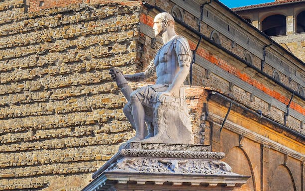 Statue of a seated figure on a historic building in Florence, Italy.