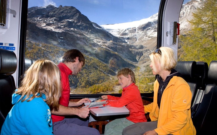 Family enjoying Bernina Express train ride through snowy St Moritz Alps.