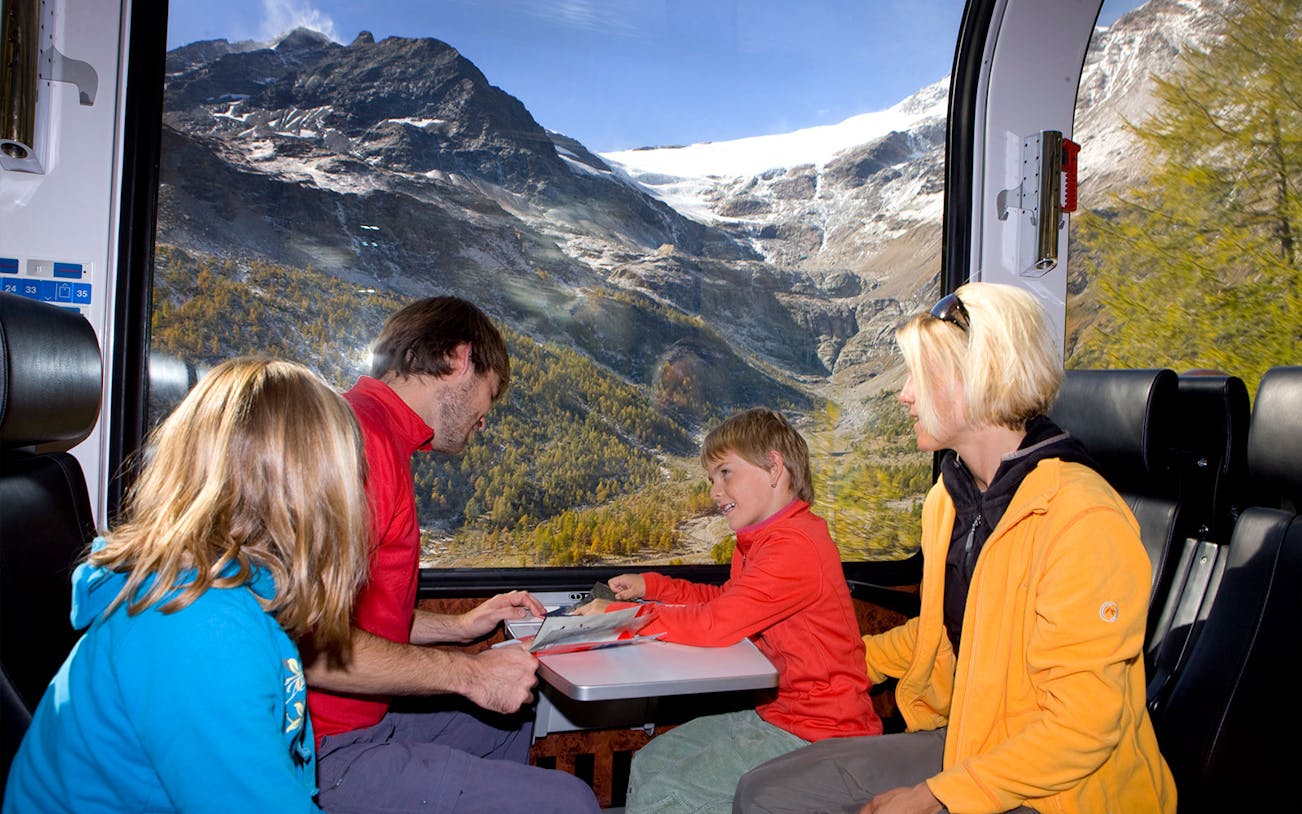 Family enjoying Bernina Express train ride through snowy St Moritz Alps.