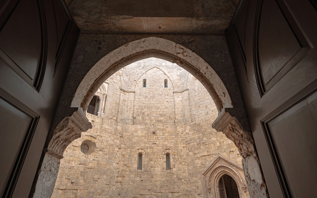 View of Castel del Monte's stone courtyard through an arched doorway, Italy.