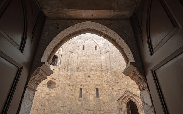 View of Castel del Monte's stone courtyard through an arched doorway, Italy.