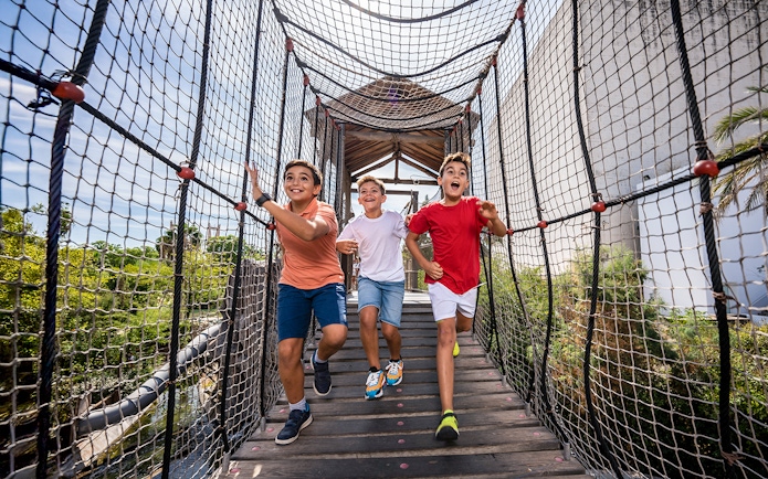 Children running on a rope bridge at Isla Mágica adventure park.