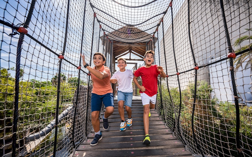 Children running on a rope bridge at Isla Mágica adventure park.