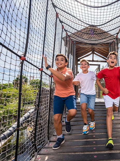 Children running on a rope bridge at Isla Mágica adventure park.