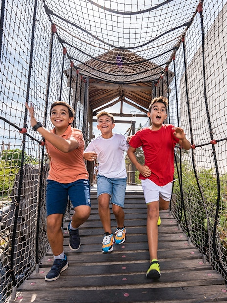 Children running on a rope bridge at Isla Mágica adventure park.