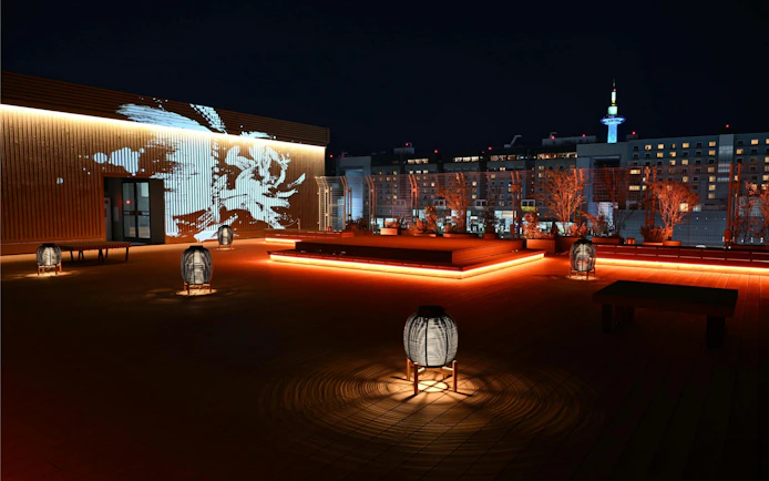 Rooftop view of DRUM TAO Theater Kyoto with illuminated lanterns and city skyline.