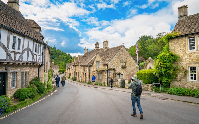 Quaint street in Cotswold village with stone cottages and people walking.