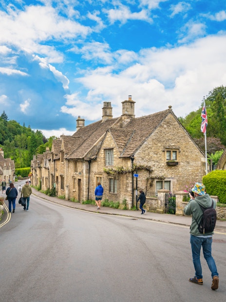 Quaint street in Cotswold village with stone cottages and people walking.