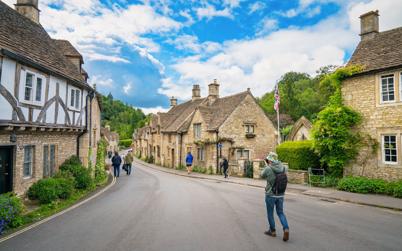 Quaint street in Cotswold village with stone cottages and people walking.
