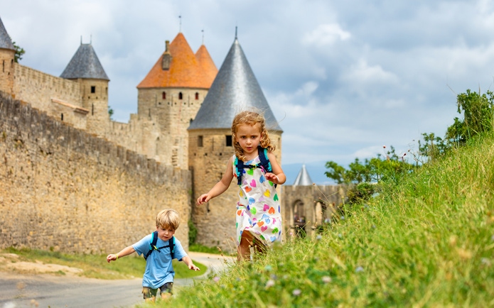 Children exploring near the walls of Cité de Carcassonne, France, with Comtal Castle in view.