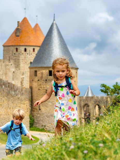 Children exploring near the walls of Cité de Carcassonne, France, with Comtal Castle in view.