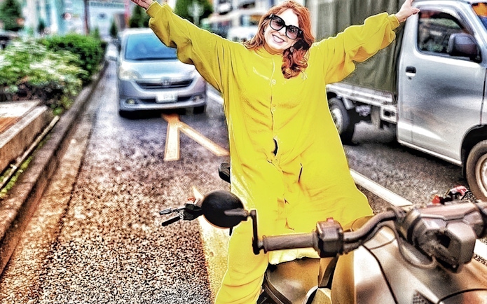 Woman in yellow onesie on go-kart with arms outstretched on Tokyo street.