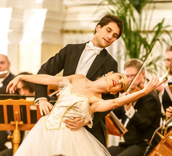 Dancers performing in a classical concert setting in Vienna, with musicians playing in the background.
