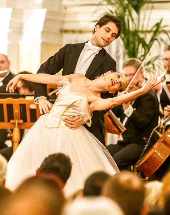 Dancers performing in a classical concert setting in Vienna, with musicians playing in the background.