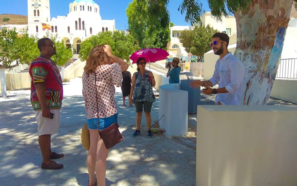 Tour guide explaining to visitors near a church in Santorini during a day tour.