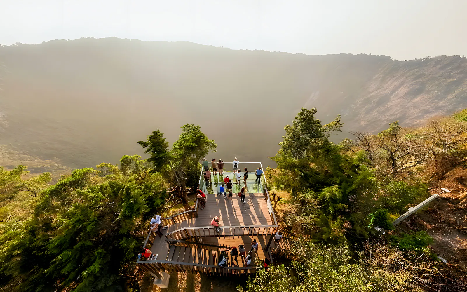Visitors on a viewing platform overlooking El Boquerón Volcano crater, surrounded by lush greenery.