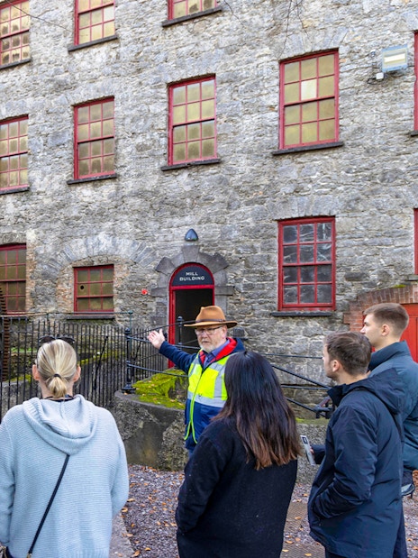 Tour group at Midleton Distillery's historic waterwheel with guide explaining its significance.