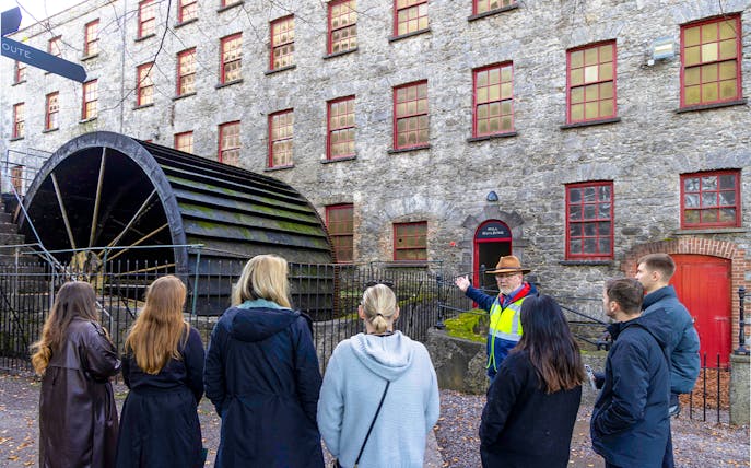 Tour group at Midleton Distillery's historic waterwheel with guide explaining its significance.