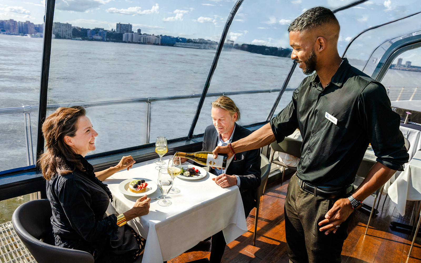 Couple dining on New Jersey Signature Cruise with waiter serving wine.