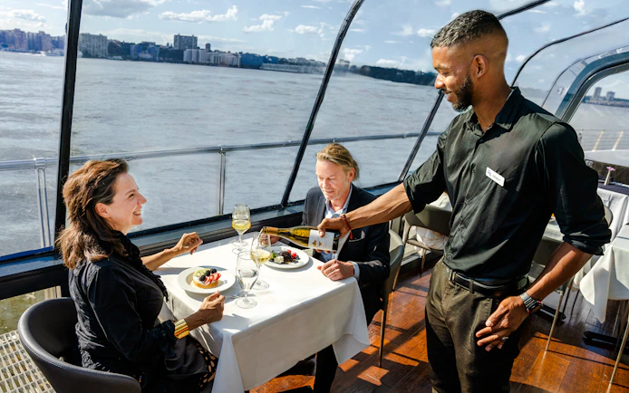 Couple dining on New Jersey Signature Cruise with waiter serving wine.