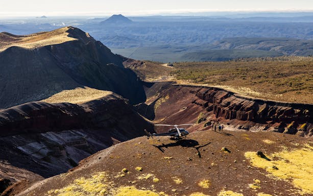 Helicopter on Mount Tarawera summit with tourists, showcasing volcanic landscape and distant peaks.