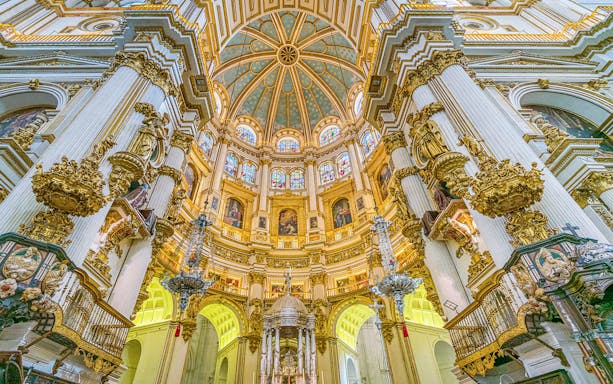 Granada Cathedral main nave with ornate columns and stained glass windows.