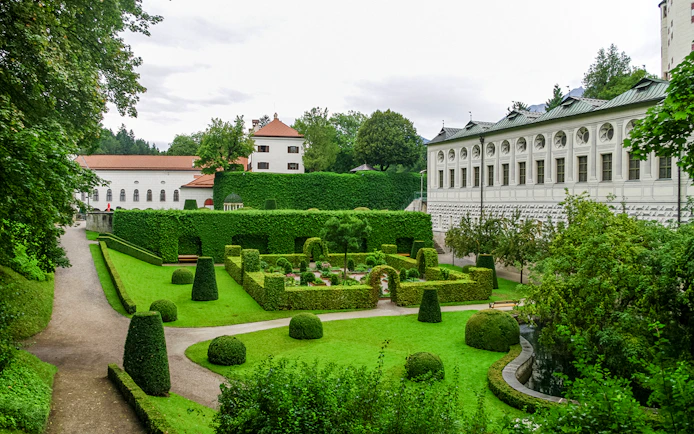Ambras Castle Innsbruck gardens with manicured hedges and historic architecture.