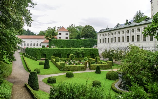 Ambras Castle Innsbruck gardens with manicured hedges and historic architecture.