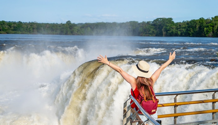 Backshot of tourist at Iguazu Falls with arms raised towards the sun, Argentina-Brazil border.